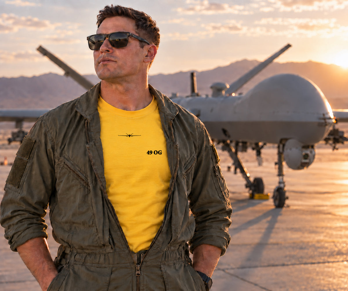 Member wearing the yellow 49 OG morale shirt beneath an open flight suit in front of an MQ-9 aircraft.