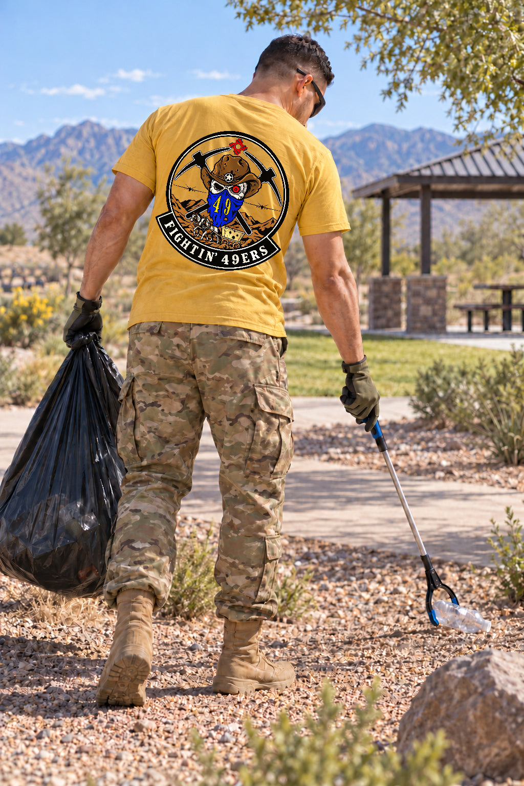 Rear view of a member collecting litter while wearing the yellow Fightin’ 49ers morale shirt and camouflage trousers.